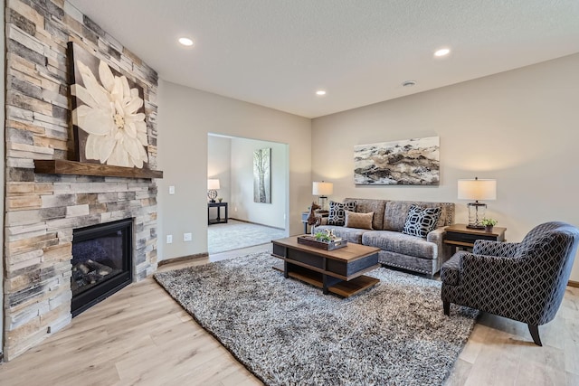 living area with light wood finished floors, a stone fireplace, recessed lighting, and a textured ceiling