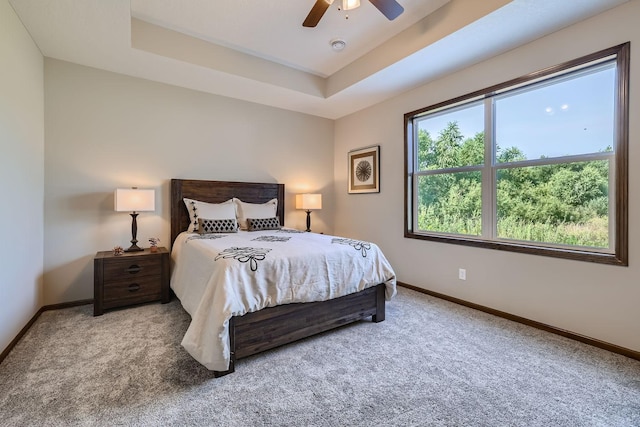 carpeted bedroom featuring ceiling fan, a tray ceiling, and baseboards