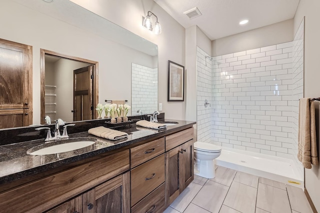 full bathroom with a tile shower, visible vents, toilet, and a sink