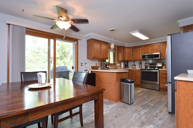 kitchen featuring pendant lighting, crown molding, light hardwood / wood-style flooring, ceiling fan, and appliances with stainless steel finishes