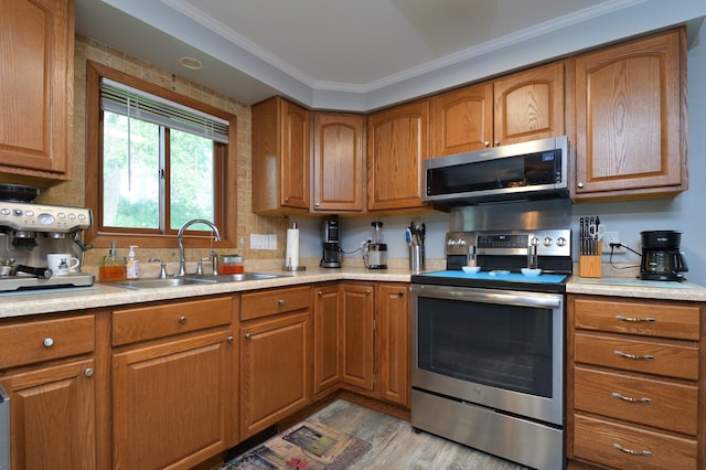 kitchen with stainless steel appliances, ornamental molding, sink, and light hardwood / wood-style floors