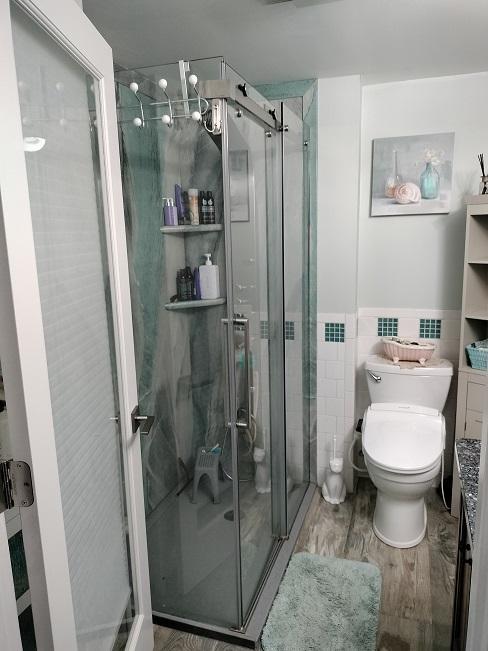 bathroom with a shower with door, wood-type flooring, tile walls, and toilet