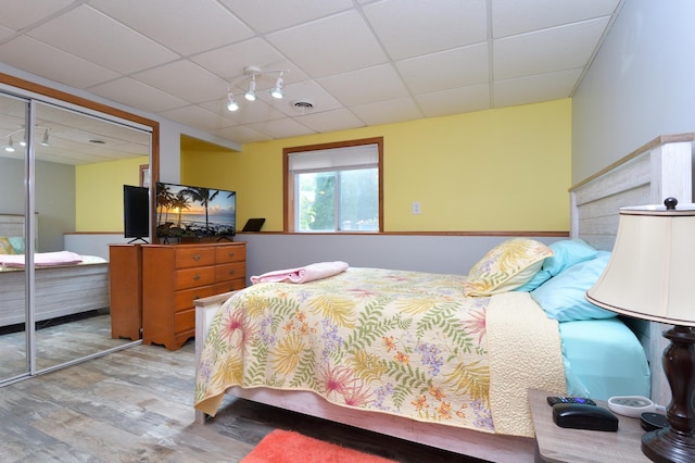 bedroom with a drop ceiling, light hardwood / wood-style floors, and a closet