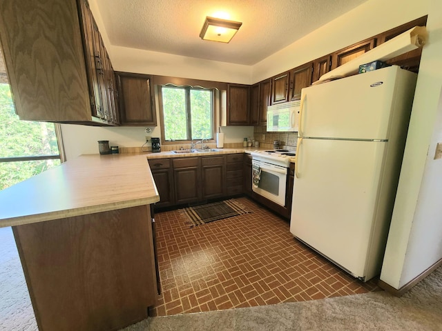 kitchen featuring dark brown cabinetry, sink, white appliances, and kitchen peninsula