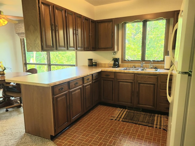 kitchen featuring dark brown cabinetry, sink, white refrigerator, kitchen peninsula, and ceiling fan