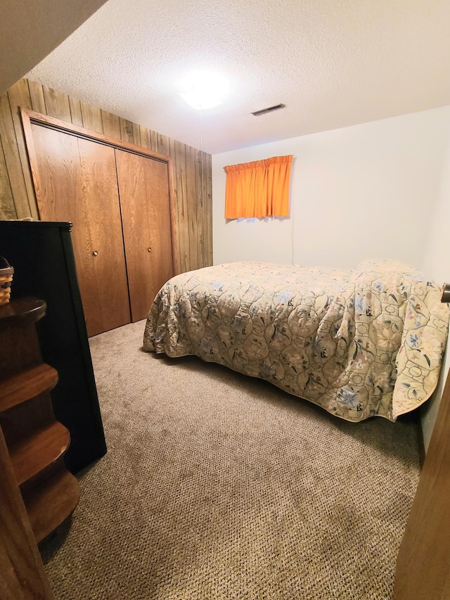 carpeted bedroom with a closet, wooden walls, and a textured ceiling