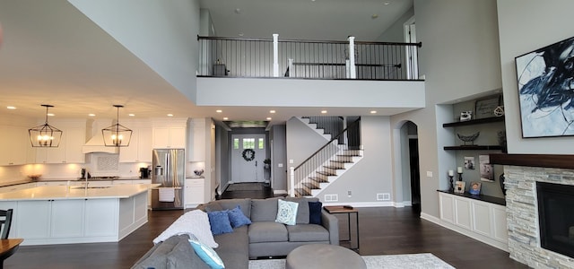 living room featuring dark hardwood / wood-style flooring, built in shelves, a chandelier, a high ceiling, and a stone fireplace