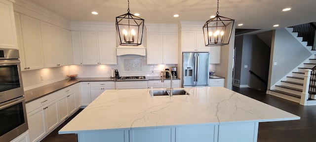 kitchen with sink, stainless steel appliances, an island with sink, dark stone counters, and pendant lighting