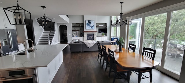 dining space with dark hardwood / wood-style flooring, a stone fireplace, a notable chandelier, and sink