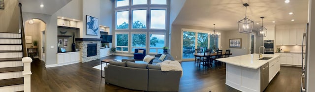 living room featuring sink, an inviting chandelier, a high ceiling, dark hardwood / wood-style floors, and a stone fireplace