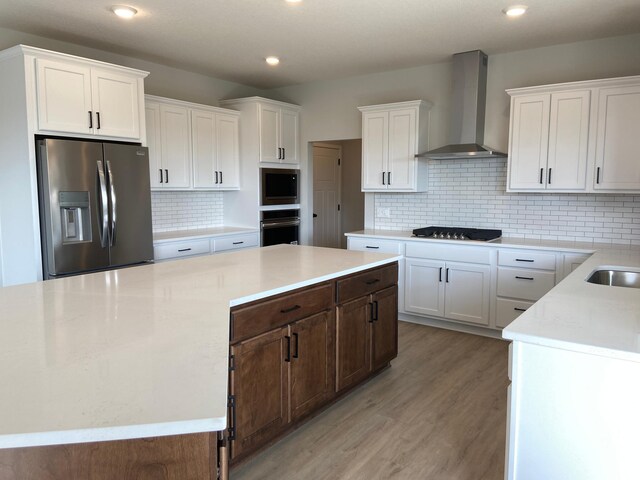 kitchen featuring backsplash, light hardwood / wood-style floors, wall chimney exhaust hood, and appliances with stainless steel finishes