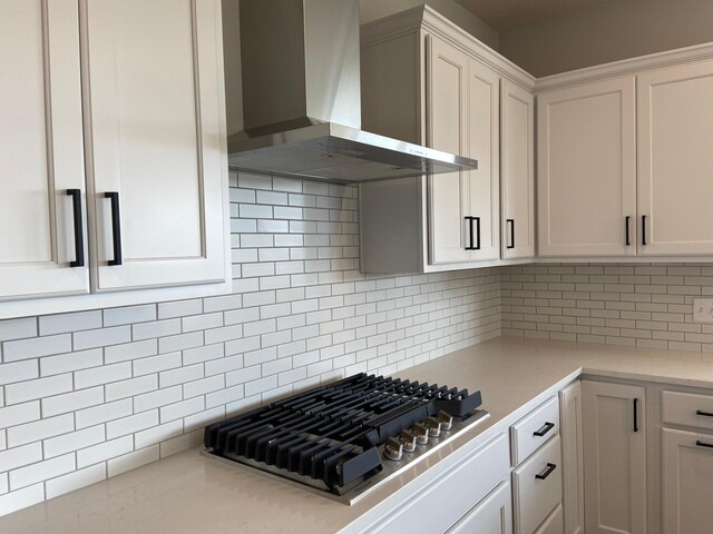 kitchen with stainless steel gas cooktop, white cabinetry, backsplash, and wall chimney range hood