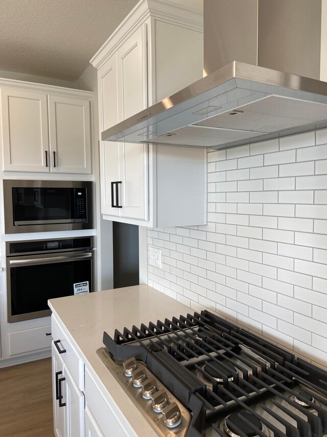 kitchen featuring white cabinetry, wall chimney range hood, appliances with stainless steel finishes, backsplash, and dark wood-type flooring