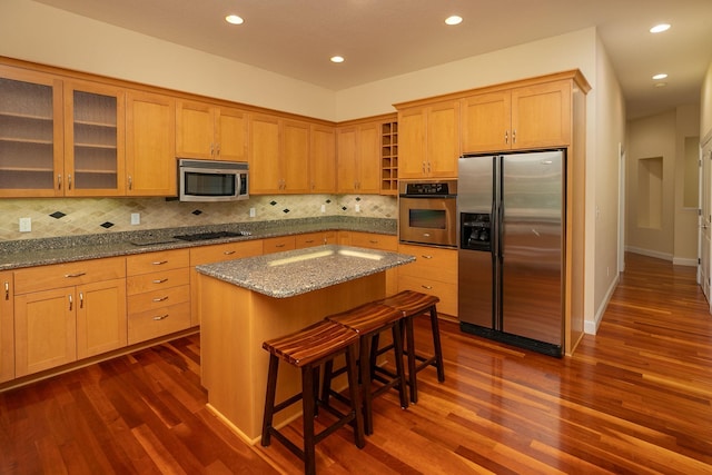 kitchen with dark wood-type flooring, appliances with stainless steel finishes, light stone counters, and a kitchen island