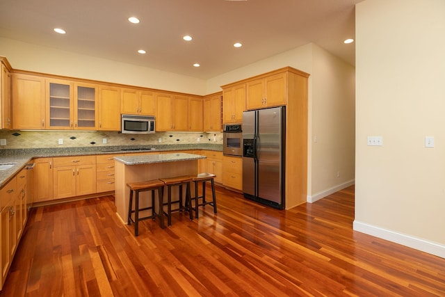 kitchen with a breakfast bar area, a center island, appliances with stainless steel finishes, and dark hardwood / wood-style flooring