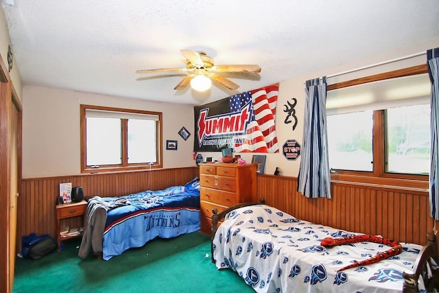 carpeted bedroom featuring wooden walls, a textured ceiling, and ceiling fan