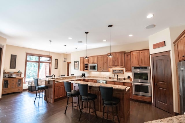 kitchen featuring hanging light fixtures, dark hardwood / wood-style floors, appliances with stainless steel finishes, kitchen peninsula, and a breakfast bar area