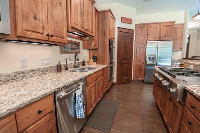 kitchen with appliances with stainless steel finishes, dark hardwood / wood-style flooring, light stone counters, and sink