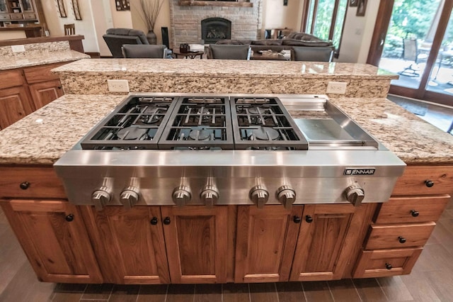 kitchen featuring a brick fireplace, light stone countertops, dark wood-type flooring, and stainless steel gas cooktop