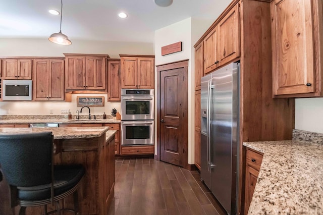 kitchen with light stone counters, stainless steel appliances, dark wood-type flooring, sink, and pendant lighting