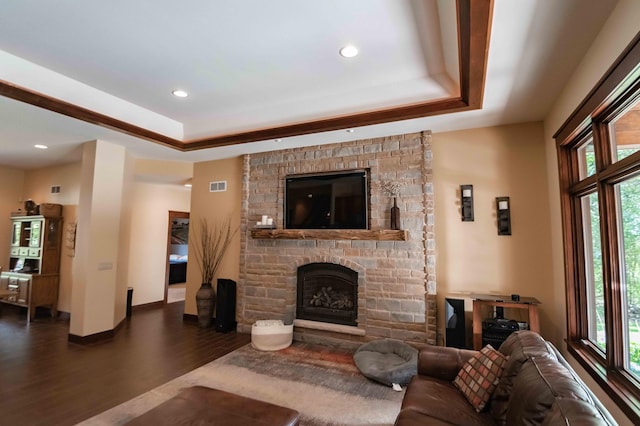 living room with a tray ceiling, a fireplace, plenty of natural light, and dark wood-type flooring