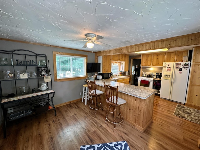 kitchen featuring kitchen peninsula, wooden walls, wood-type flooring, and white appliances