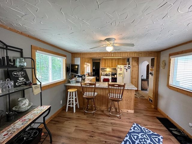 kitchen featuring a kitchen bar, kitchen peninsula, crown molding, and white refrigerator with ice dispenser