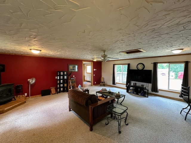 carpeted living room with ceiling fan, a wood stove, and a textured ceiling