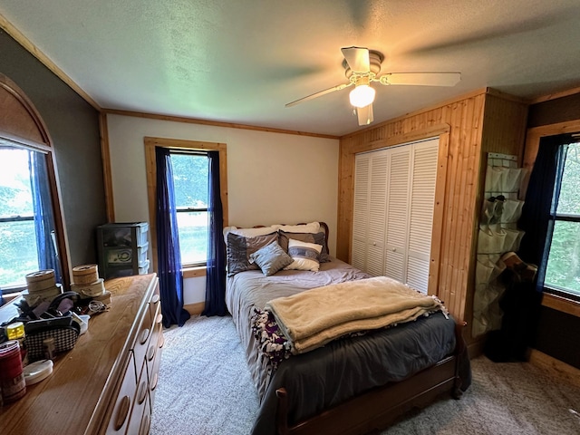 carpeted bedroom with a wood stove, ceiling fan, crown molding, a textured ceiling, and a closet