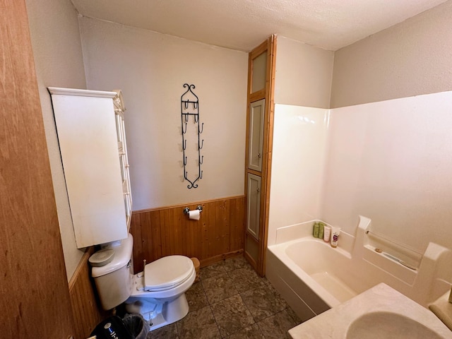 bathroom with a tub to relax in, toilet, and wood walls