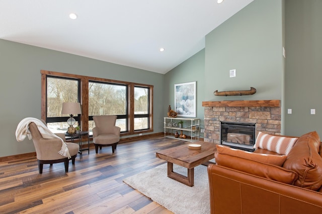 living room featuring hardwood / wood-style flooring, a stone fireplace, and high vaulted ceiling