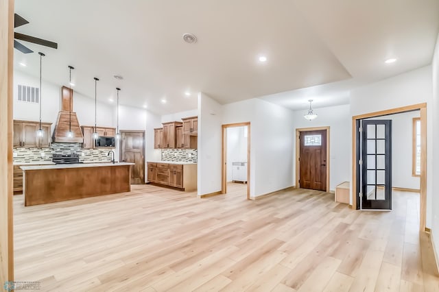 kitchen with backsplash, a spacious island, hanging light fixtures, light hardwood / wood-style flooring, and custom range hood