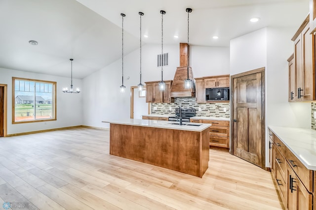 kitchen with a kitchen island with sink, an inviting chandelier, decorative light fixtures, and light wood-type flooring