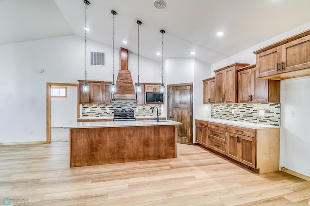 kitchen featuring custom range hood, electric stove, pendant lighting, a center island with sink, and light hardwood / wood-style floors