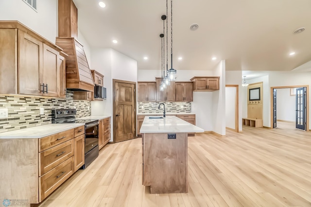 kitchen with pendant lighting, light hardwood / wood-style flooring, a kitchen island with sink, and black appliances