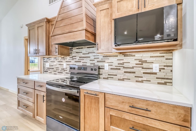 kitchen featuring premium range hood, decorative backsplash, stainless steel electric range oven, light wood-type flooring, and light stone counters