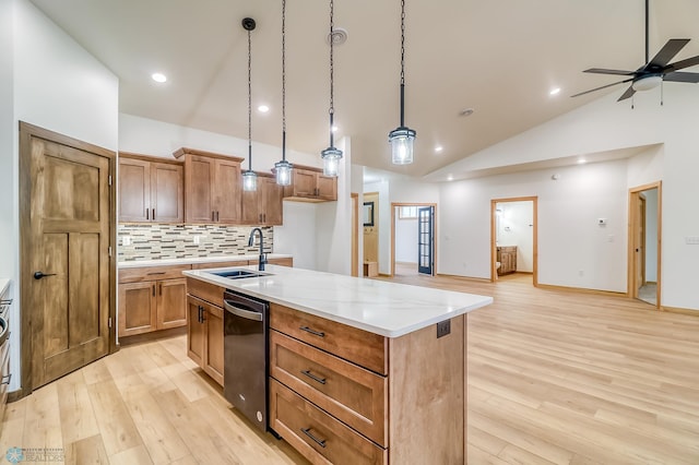 kitchen featuring a kitchen island with sink, sink, stainless steel dishwasher, decorative light fixtures, and light hardwood / wood-style floors