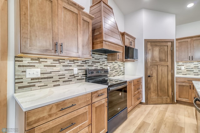 kitchen featuring custom exhaust hood, backsplash, light wood-type flooring, black / electric stove, and light stone counters