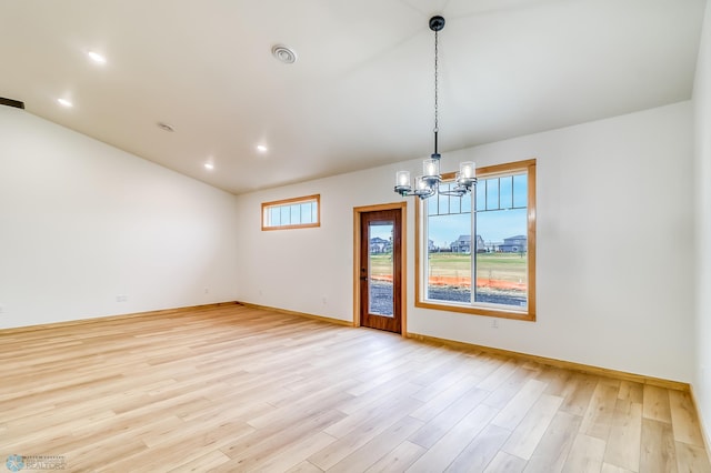 spare room featuring a notable chandelier, a healthy amount of sunlight, and light hardwood / wood-style floors