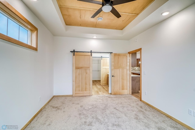 unfurnished bedroom featuring ceiling fan, a barn door, a raised ceiling, and light carpet