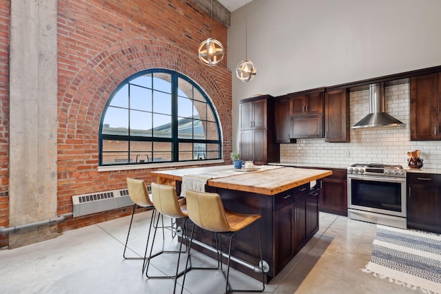 kitchen with butcher block counters, gas stove, dark brown cabinets, a kitchen island, and wall chimney range hood