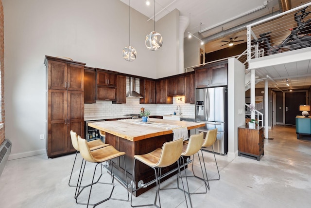 kitchen featuring dark brown cabinetry, butcher block countertops, backsplash, and stainless steel fridge