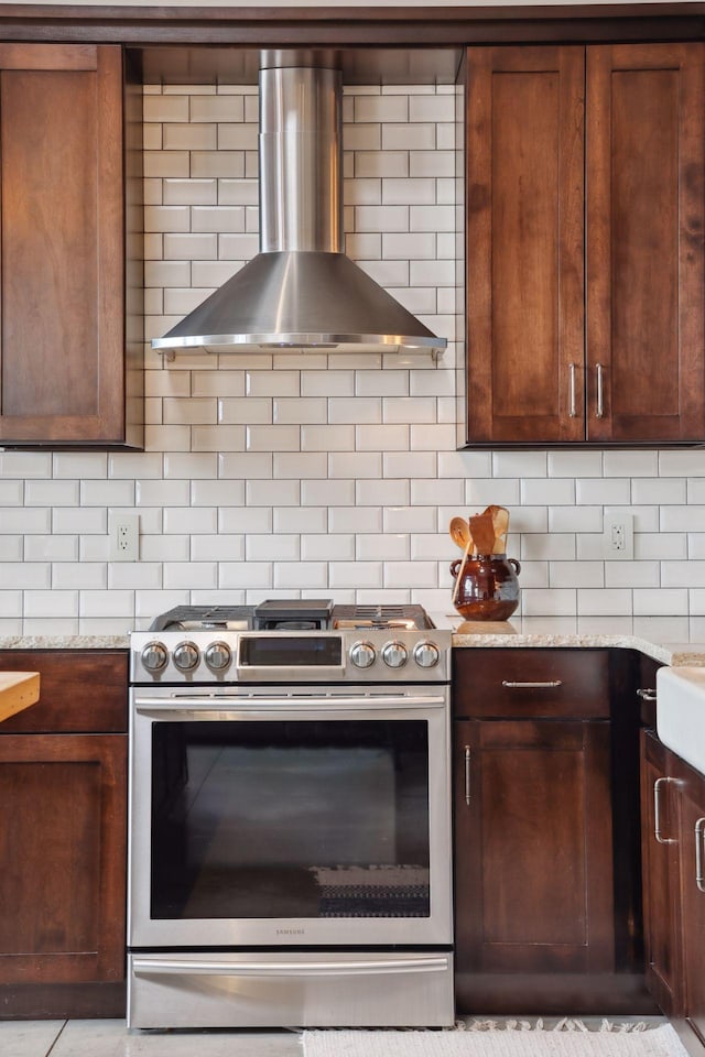 kitchen featuring stainless steel range with gas stovetop, backsplash, light stone counters, and wall chimney exhaust hood