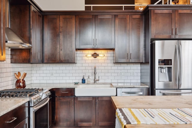 kitchen with sink, decorative backsplash, light stone counters, stainless steel appliances, and dark brown cabinets