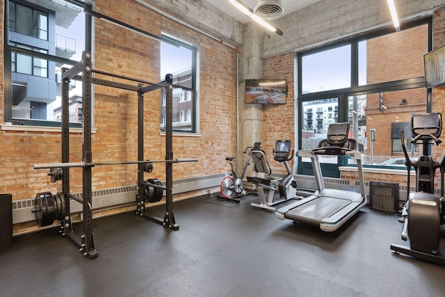 exercise room featuring a high ceiling, a healthy amount of sunlight, and brick wall