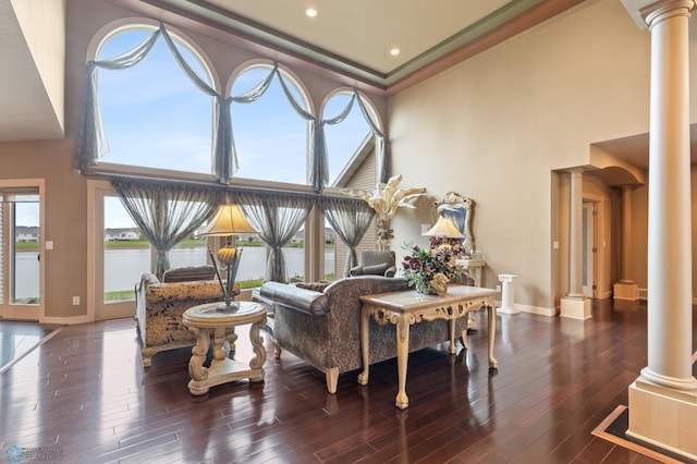 living room featuring decorative columns, a water view, dark wood-type flooring, and a towering ceiling