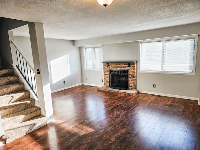 unfurnished living room with a brick fireplace, stairway, baseboards, and wood finished floors