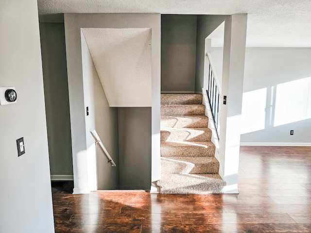 stairway featuring a textured ceiling, baseboards, and wood finished floors