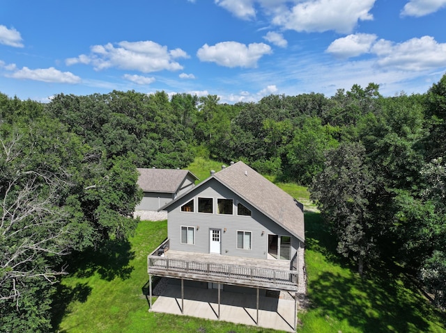 back of house with a deck, a shingled roof, a lawn, and a wooded view