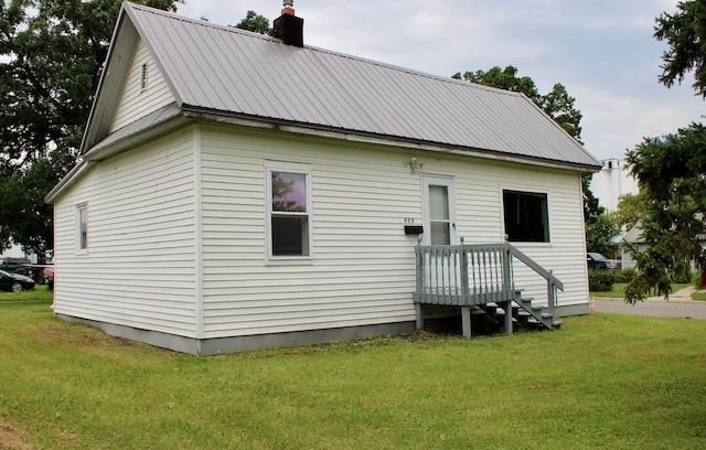 back of property featuring metal roof, a yard, and a chimney